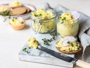 Tartlets with egg pate or salad and radish and thyme on light stone background. Egg dip in glass...