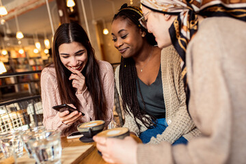 Three young multiethnic female friends spending time together at a coffee shop.