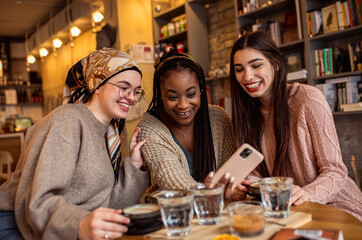 Three young multiethnic female friends spending time together at a coffee shop.