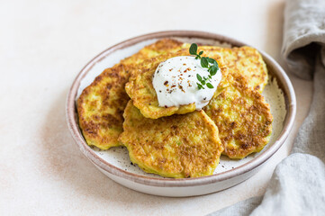 Vegetable fritters or pancakes with yoghurt or cream sour dressing and herbs. Cabbage or zucchini fritters on ceramic plate. Healthy vegetarian food.