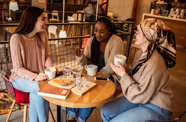 Three young multiethnic female friends spending time together at a coffee shop.