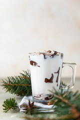 Glass cup with hot chocolate or cocoa drink and cinnamon sticks with anise, light concrete background.