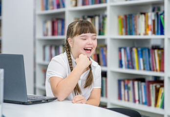 Portrait of a laughing  young girl with syndrome down at library. Education for disabled children concept