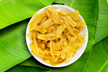 Banana slice chips in white plate on banana leaves background. © Bowonpat