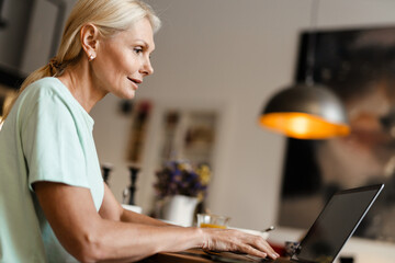 Blonde mature woman typing on laptop while sitting at table
