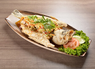 Fototapeta na wymiar deep fried crispy whole grouper fish with mango salad dressing on wood background asian halal menu
