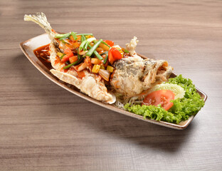 deep fried crispy whole grouper fish with vegetables in sweet and sour sauce on wood background asian halal menu