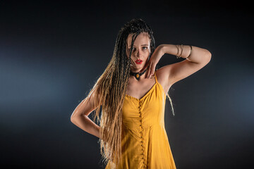 Mystic ancient queen goddess wearing a yellow dress on an isolated black studio background. Female feminist wearing braids and posing in a studio.