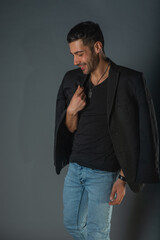 Handsome fashionable model in a black t-shirt with a jacket on his shoulders posing in a studio