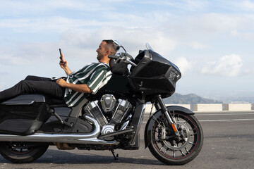 Fototapeta na wymiar Chico acostado en una moto negra escribiendo un mensaje de texto.