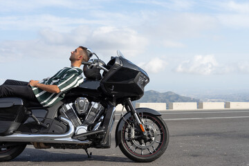 Fototapeta na wymiar Chico relajado acostado en una moto con la carretera y cielo de fondo.