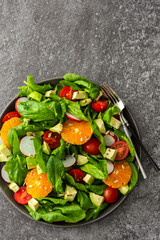 Delicious healthy salad of spinach leaves, tangerine and avocado slices, tomato and radish with seeds, salad in a plate close-up with forks, top view, copy space