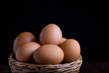 Close up of fresh chicken eggs in wicker basket on wooden table in the kitchen with dark background.