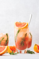 Cold refreshing grapefruit smoothie with rosemary and ice in glass close up, grapefruit wedges and rosemary sprigs on the table, home party