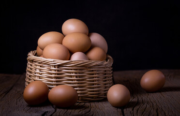 Chicken eggs in wicker basket on wooden table with dark background.