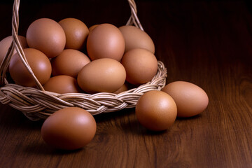 Chicken eggs in wicker basket on wooden table with dark background.