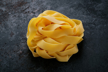 Raw pappardelle pasta on a black stone background. Fresh uncooked egg pasta