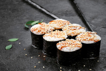Maki Japanese roll with smoked eel and sesame seeds on stone. Unagi sushi-roll with chopstick, selective focus