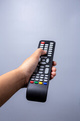 woman's hand holding TV remote control on gray background.