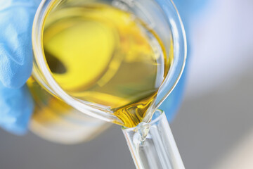 Scientist chemist pouring yellow oil from glass jar into test tube closeup
