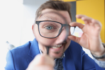Man with glasses holding magnifying glass in front of his eye closeup