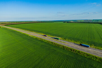 multicolored trucks on the higthway sunset. cargo delivery driving on asphalt road along the green fields with goods. seen from the air. Aerial view landscape. drone photography. convoys with cargo