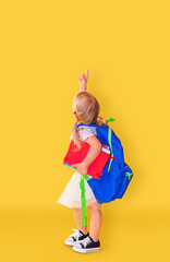 Little girl with pointing finger up at yellow background. Back to school.