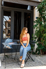 Portrait of a young hipster woman in glasses drinking a cup of coffee checking her smart phone on a cafe terrace, remote work, freelance concept .