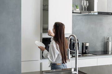 Woman opening door of kitchen cupboard with dishware