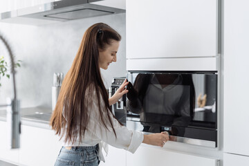 Fototapeta na wymiar Smiling beautiful woman preparing food in microwave oven