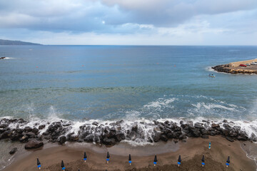 Fototapeta na wymiar Big sea waves crash against the rocks next to beach full of umbrellas
