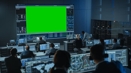 Big Green Screen Horizontal Mock Up in a Mission Control Center Room with Flight Director and Other Controllers Working on Computers. Team of Engineers Work in Monitoring Room Full of Displays.