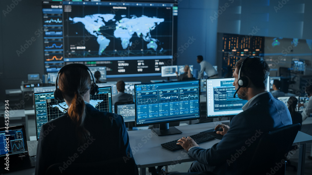 Poster Shot of Officers in a Surveillance Control Center with Police Global Map Tracking on a Big Digital Screen. Monitoring Room Employees Sit in Front of Computer Displays and Analyze Big Data.