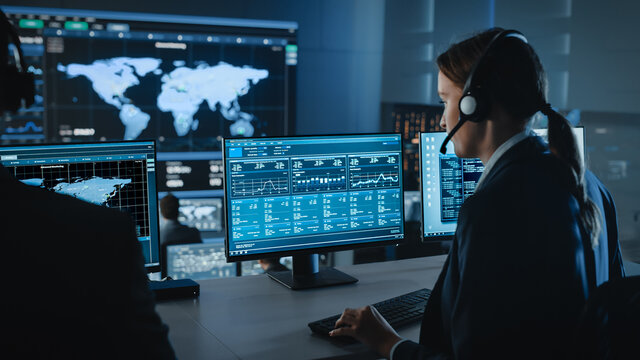 Female Specialist Works on a Computer with Live Ananlysis Feed from a Global Map on a Big Digital Screen. Employees Sit in Front of Displays with Financial Stock Market Trading Info and Big Data.