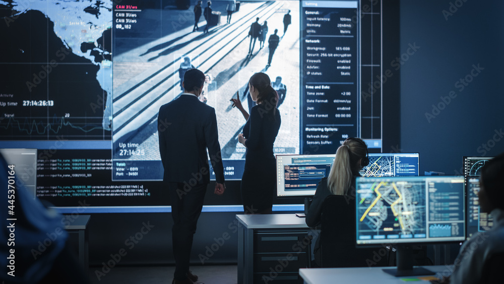 Poster male and female government officers discuss working matters next to a computer and big digital scree