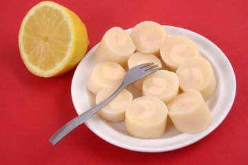 Cœurs de palmier dans une soucoupe avec une fourchette à côté d'un demi citron en gros plan sur fond rouge