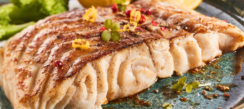 Yummy grilled fish steak with seasonings on black plate