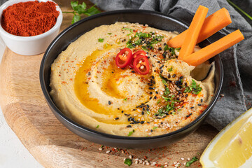 Delicious hummus in ceramic bow lwith  carrot stick dipped in hummus. Colorful snack composition on a white background.