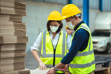 Asian male and female engineers wear protective gear and masks. Check the orderliness of the work within the warehouse.