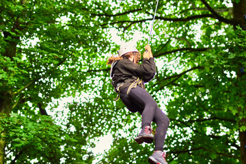 Young woman in safety equipment harness climbing and jumping from tree leap of faith on rope space...