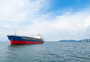 Fototapeta premium Cargo ship red blue color in the ocean and island mountain background with the blue sky and cloudy landscape