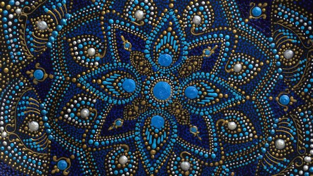 Decorative ceramic plate with black, blue and golden colors, painted plate rotating on background, closeup, top view. Decorative porcelain plate painted with acrylic paints, handwork, dot painting
