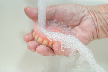 Asian senior or elderly old woman patient holding partial denture of replacement teeth.