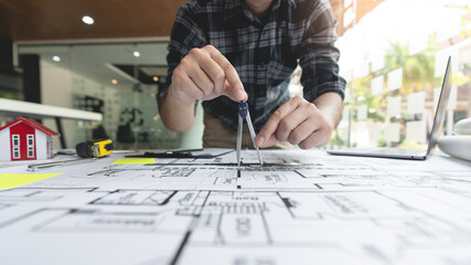 A male architect using compasses measuring and marking the scale ratio of sizes of a complicated...