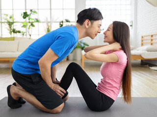 Young man helping girlfriend to do crunches at home during quarantine.