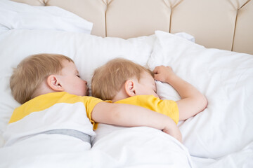 Fototapeta na wymiar two blonde boys twins sleeping hugging on white bedding