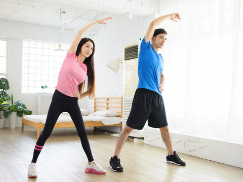 Young Couple Doing  Lateral Flexion Exercise At Home.