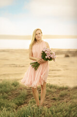 Fototapeta premium Summer mood. Romantic pensive woman in a delicate pink dress with a bouquet of roses close-up. Blonde with a bouquet of pink roses