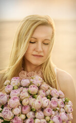 Summer mood. Romantic pensive woman in a delicate pink dress with a bouquet of roses close-up. Blonde with a bouquet of pink roses