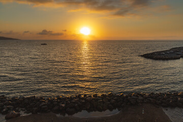 Beautiful sunset over the sea and beach full of umbrellas with sun behind clouds